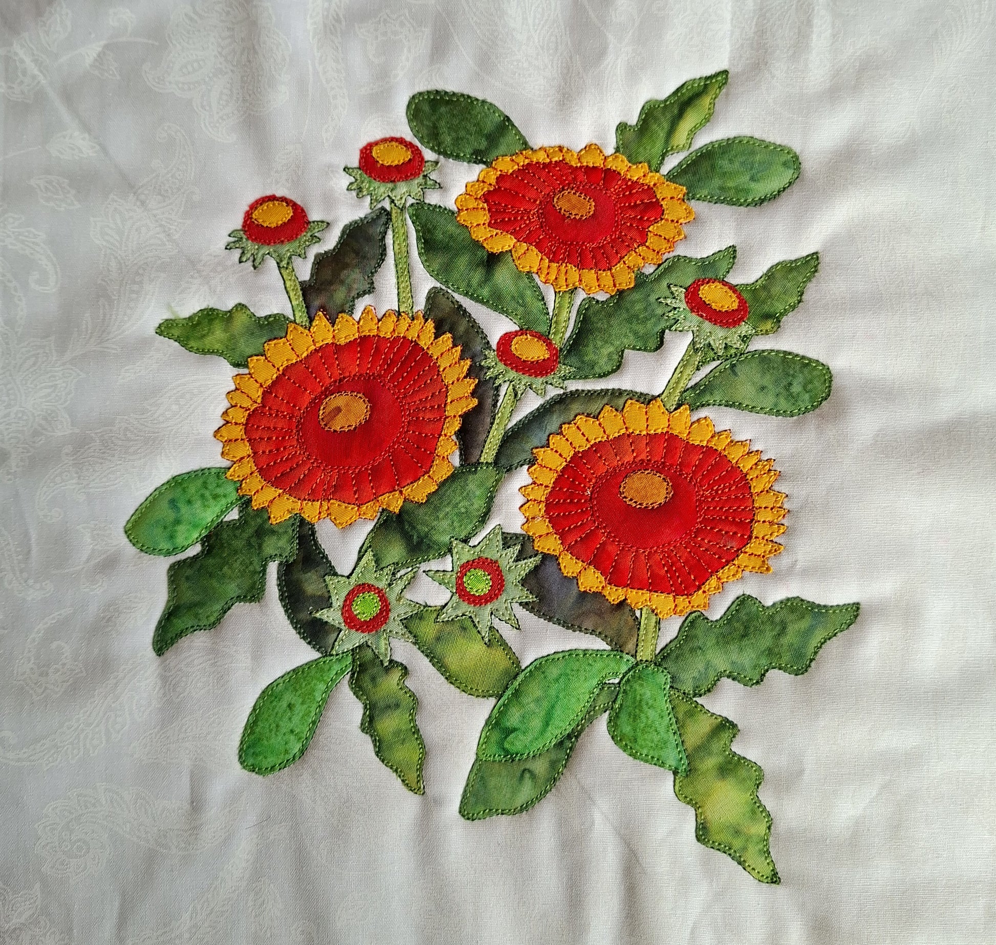 Applique design of red and yellow Gaillardia flowers with various green leaves on a white-on-white background fabric. The 82th flower applique in the BOW flower collection