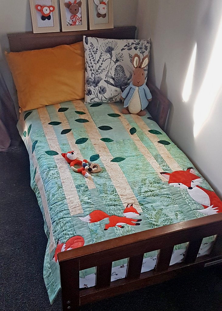 woodland theme display with fox quilt on small bed, fox rattle, hedgehog teether, Peter Rabbit crocheted toy and woodland frame set.