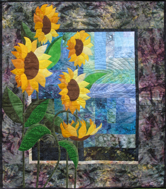 the remake of Ruth Blanchet's classic quilt pattern Simply Sunflowers using a tone of blue fabrics for the background and golden sunflowers in the foreground