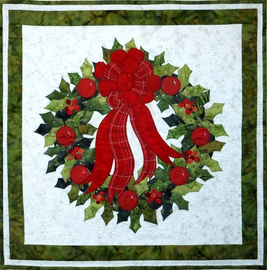 a holly wreath quilt design with appliqued holly leaves and berries. Wreath includes a large tartan ribbon at the top. The quilt is finished with two borders and binding.